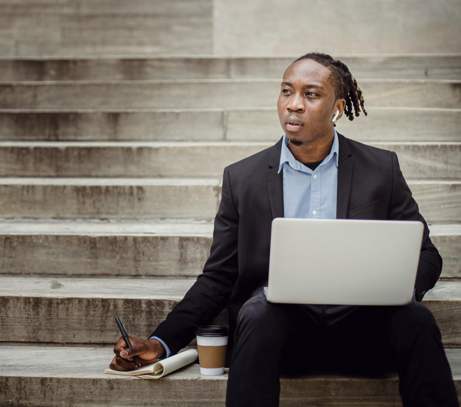 Thoughtful black worker using netbook and taking notes sitting on steps